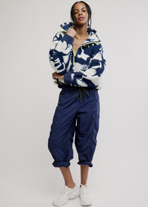 Woman wearing navy fleece jacket with white horse detail and blue pants on plain background