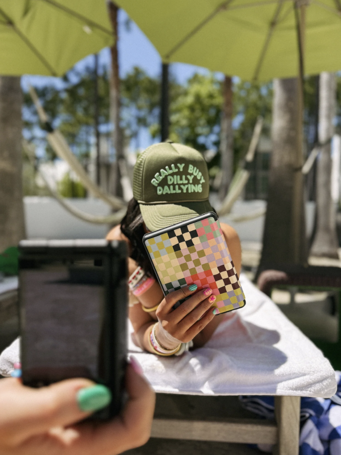Person taking a photo of a colorful phone case with a green cap in a casual setting.