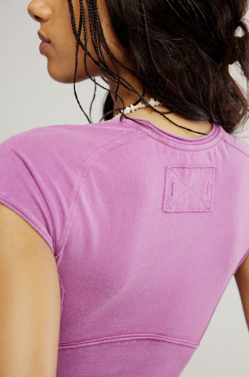 Person wearing a purple t-shirt with a visible brand logo on a plain background