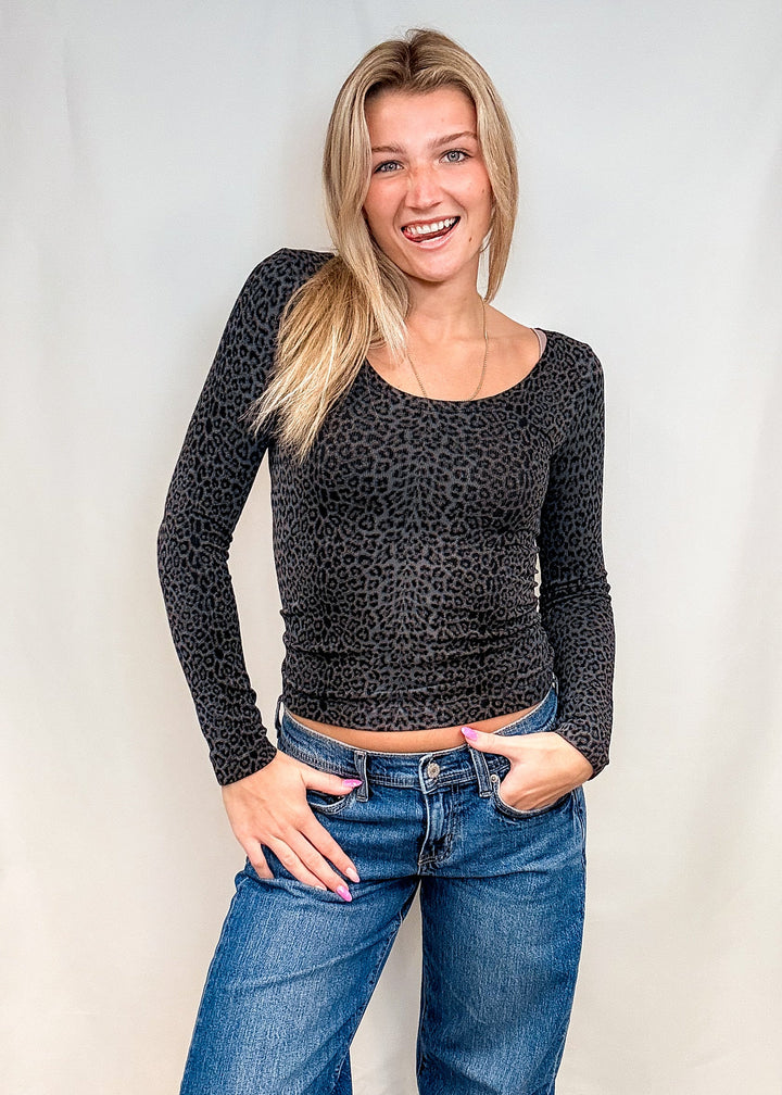 Woman wearing dark grey leopard print long sleeve with blue jeans on white background