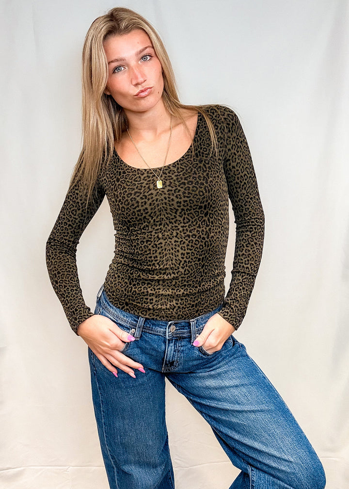 Woman wearing olive green leopard print long sleeve with blue jeans on white background