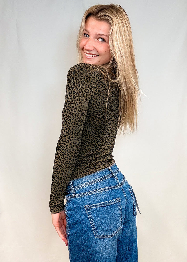Woman wearing olive green leopard print long sleeve with blue jeans on white background