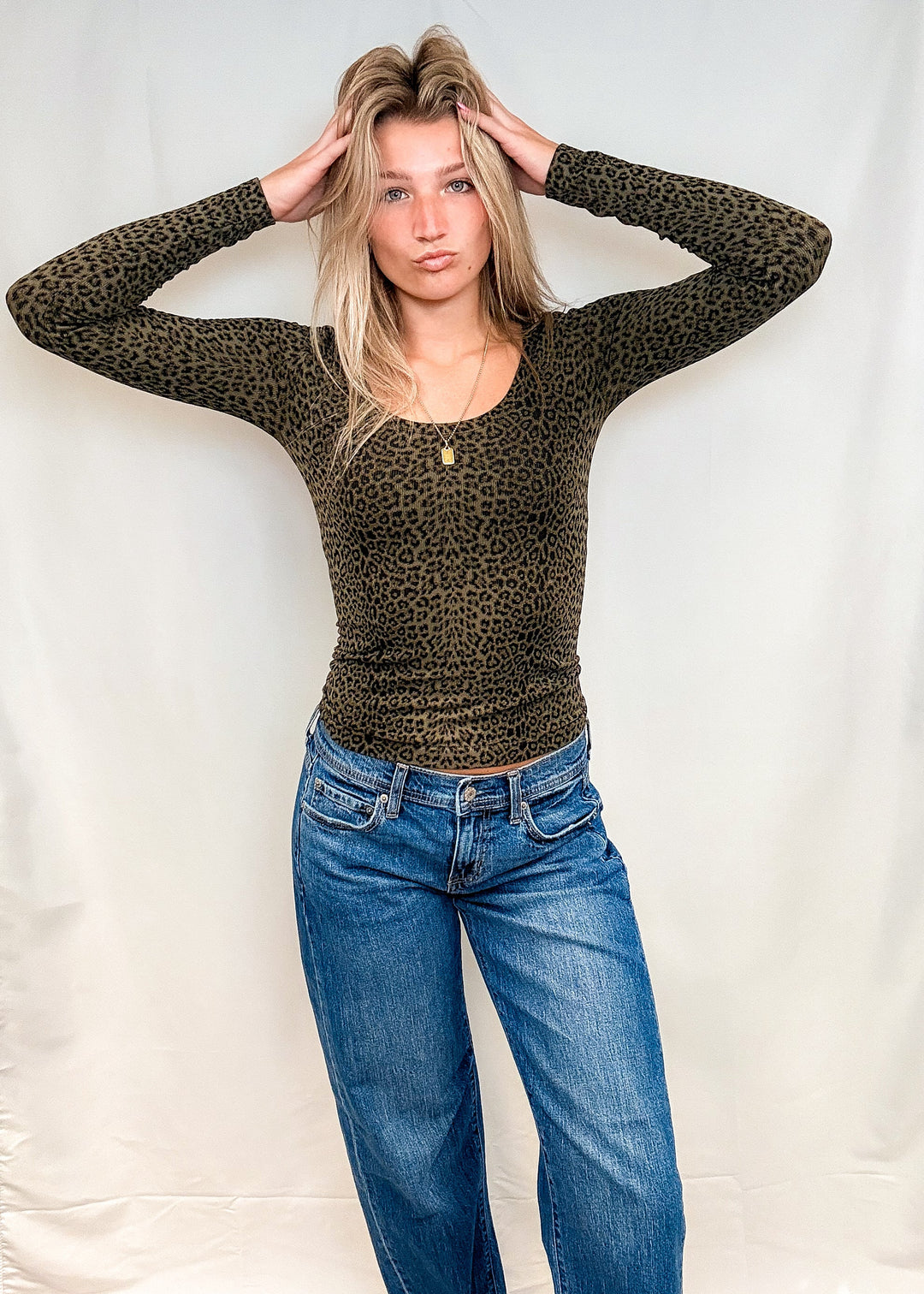 Woman wearing olive green leopard print long sleeve with blue jeans on white background