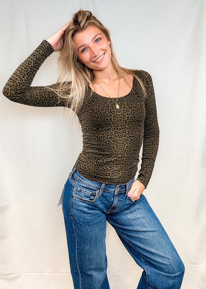 Woman wearing olive green leopard print long sleeve with blue jeans on white background