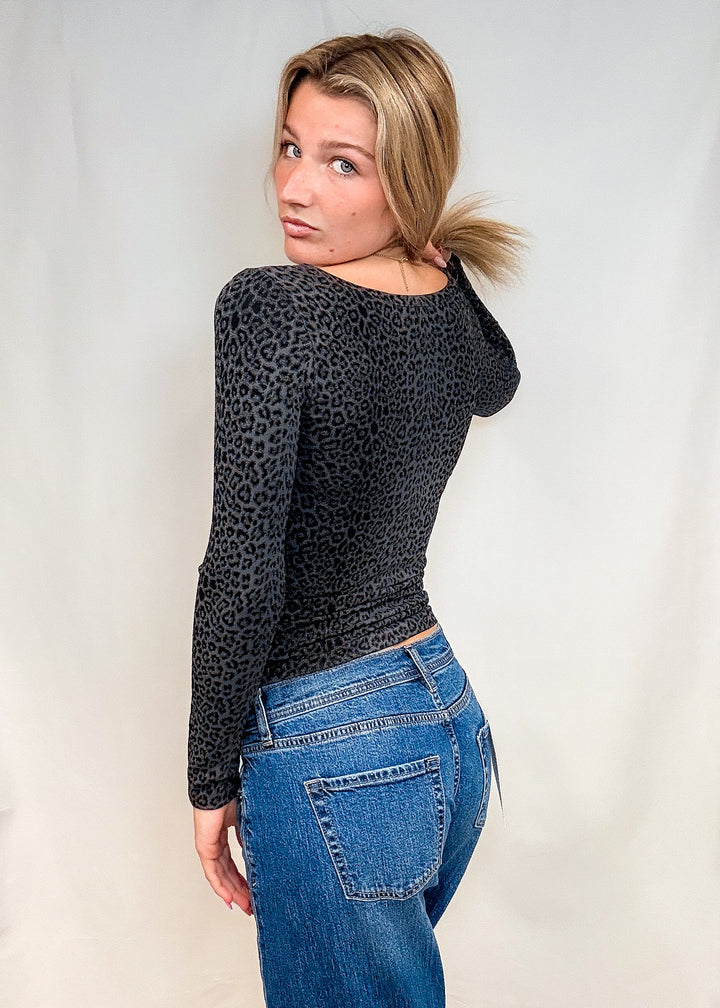 Woman wearing dark grey leopard print long sleeve with blue jeans on white background