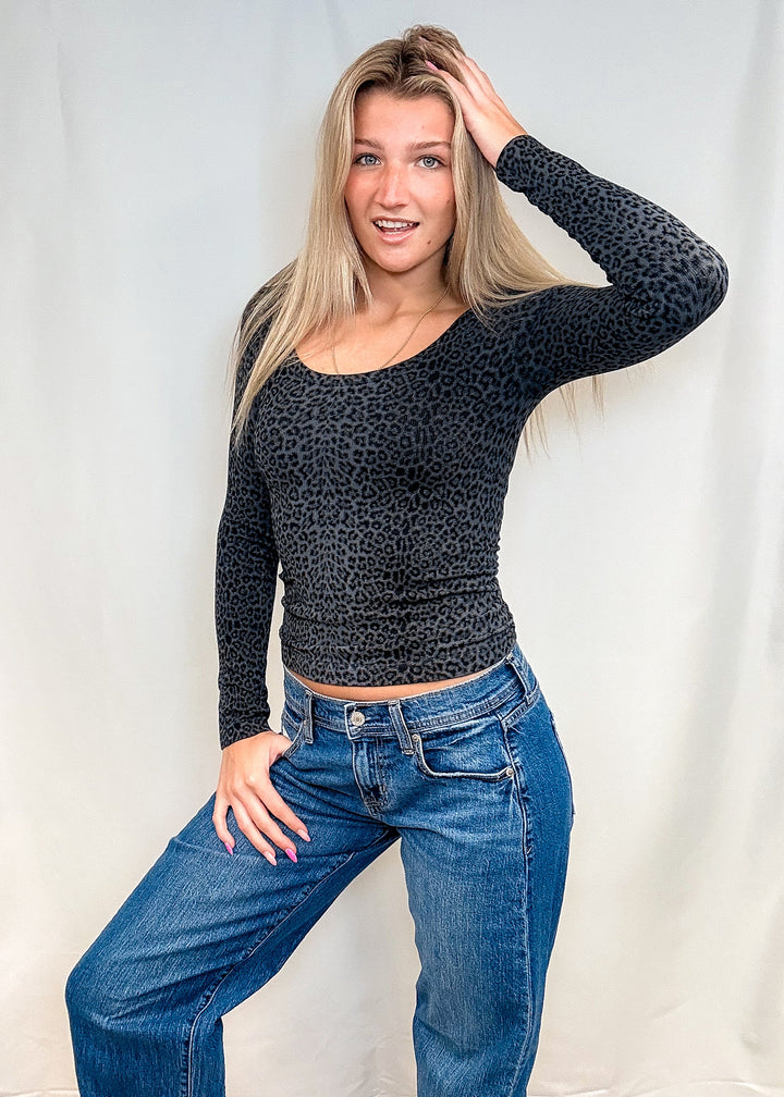 Woman wearing dark grey leopard print long sleeve with blue jeans on white background