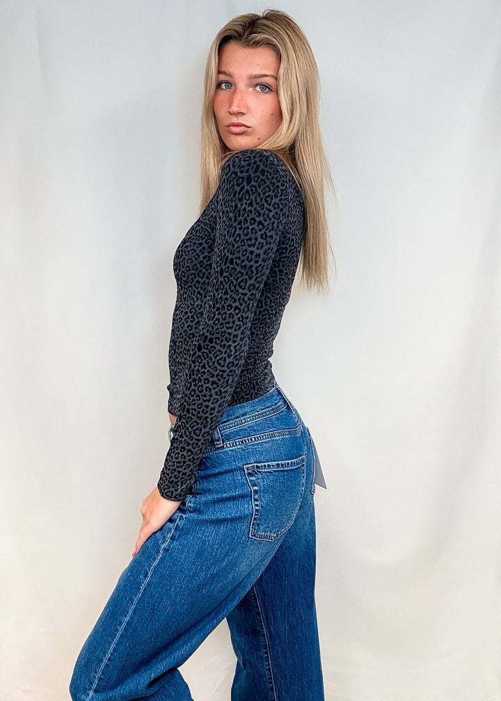 Woman wearing dark grey leopard print long sleeve with blue jeans on white background