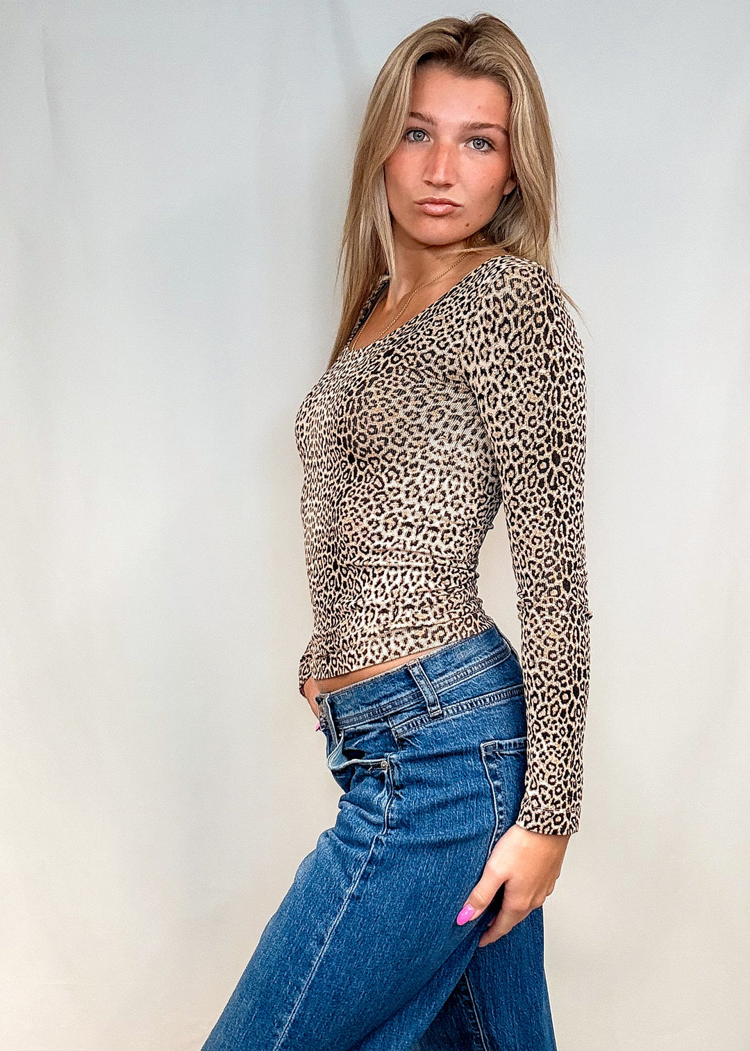 Woman wearing beige leopard print long sleeve with blue jeans on white background