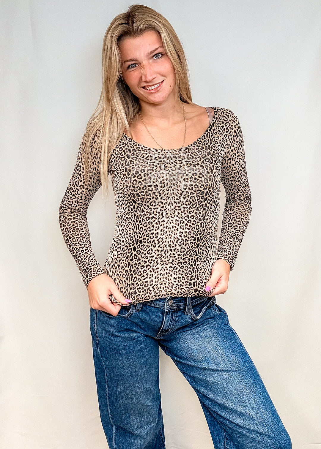 Woman wearing beige leopard print long sleeve with blue jeans on white background