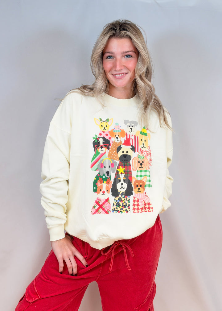 Woman wearing cream color sweatshirt with different dogs in Christmas decor and red pants on plain background