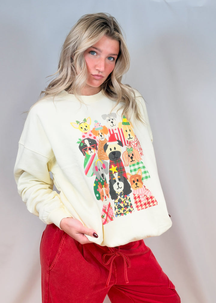 Woman wearing cream sweatshirt with multiple dogs in Christmas decor and red pants on plain background