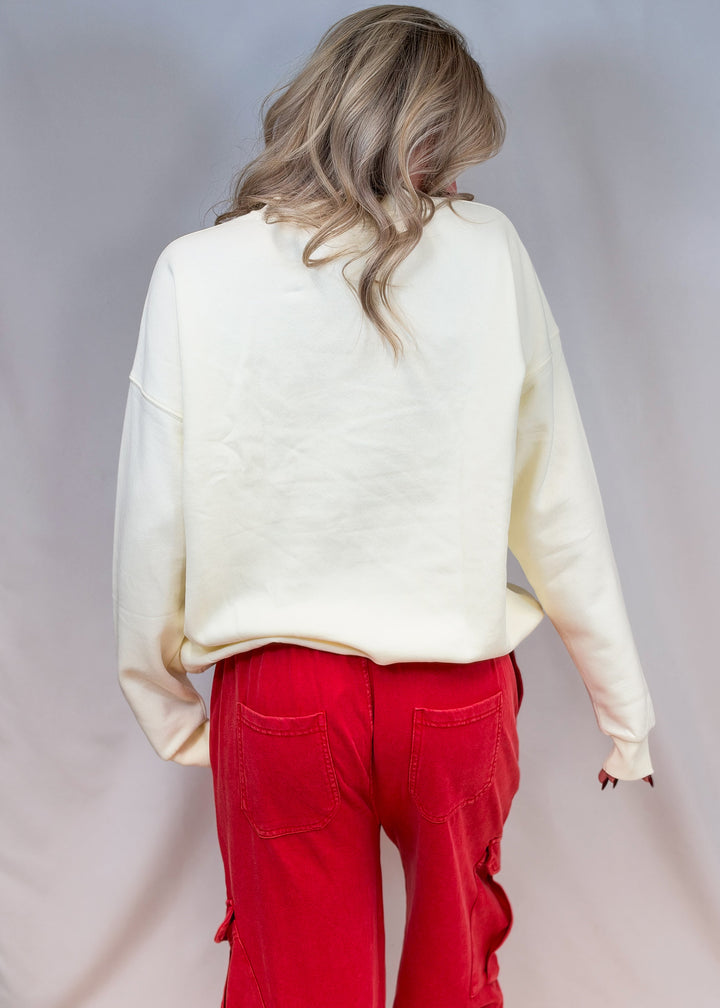 Woman shown from back wearing cream sweatshirt and red pants on plain background