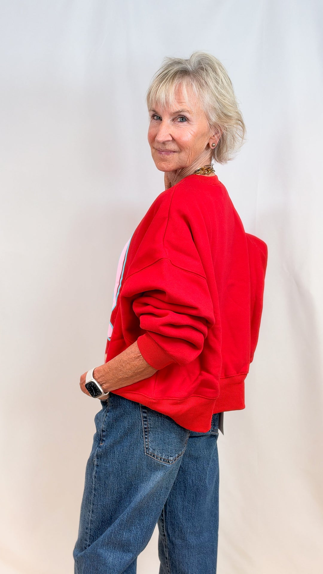 Woman wearing red sweatshirt from side view and jeans on plain background