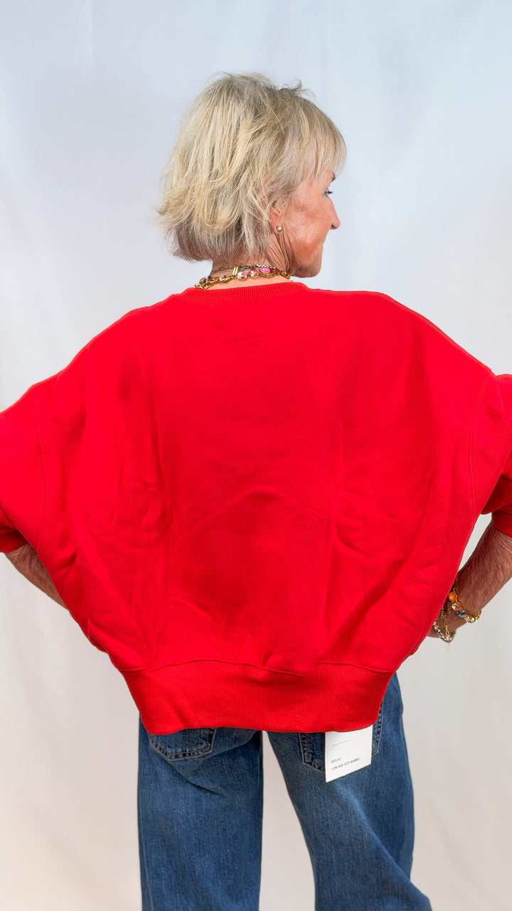 Woman shown from back wearing red sweatshirt and jeans on plain background