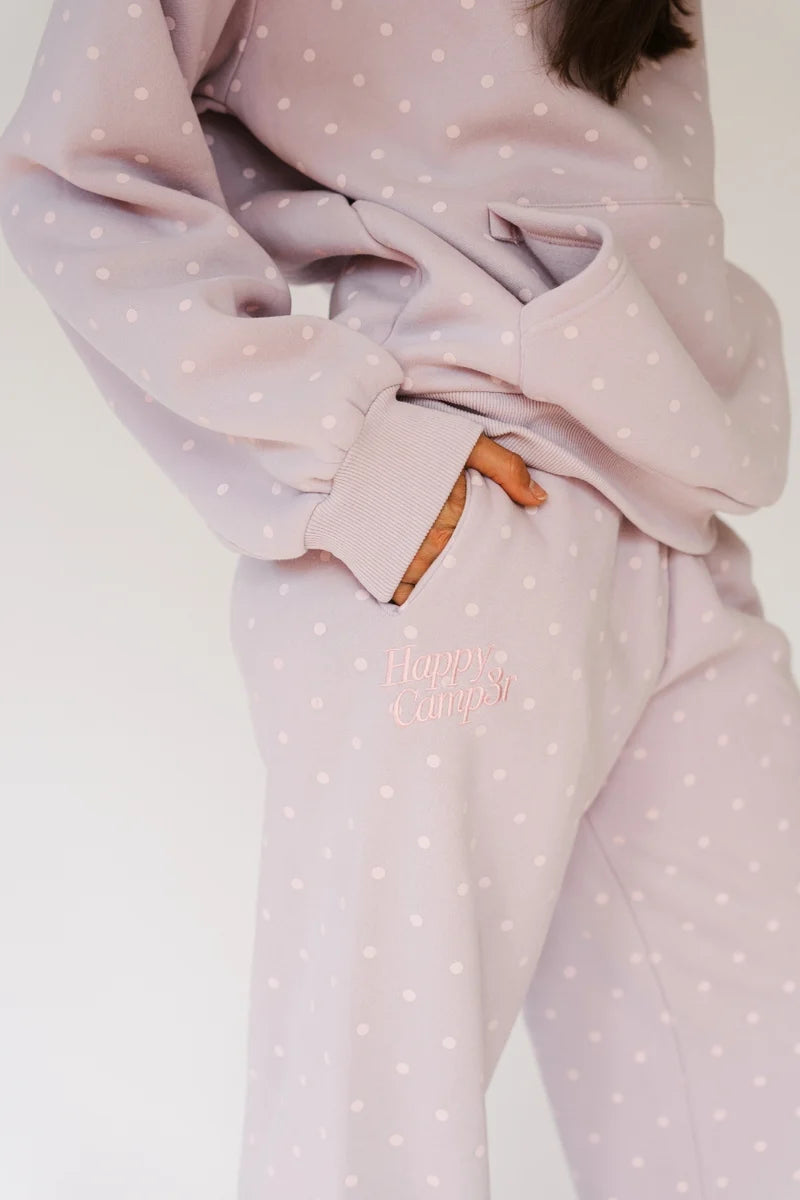 A close-up of a person wearing a matching light pink and white polka-dot lounge set, with one hand in a pocket and the words &