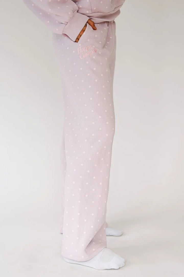 A person wearing light pink lounge pants with a white polka-dot pattern and white socks, standing against a plain light background.