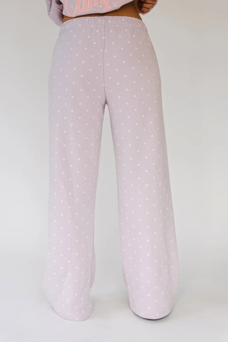 A person shown from the waist down wearing wide-leg lounge pants in a very light pink with a small white polka dot pattern, against a plain light gray studio background.