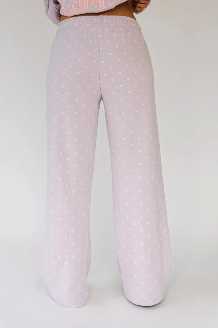 A person shown from the waist down wearing wide-leg lounge pants in a very light pink with a small white polka dot pattern, against a plain light gray studio background.