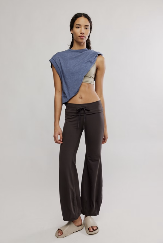 Woman wearing a blue sleeveless top and brown pants on a plain background