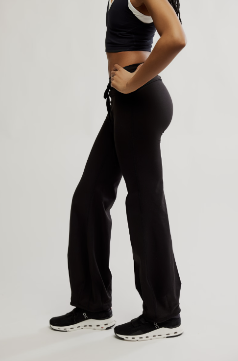 A model wearing black wide-leg sweatpants, a black crop top, and black sneakers, shown from a side profile against a light gray studio background.