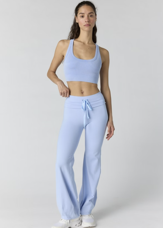 Woman wearing light blue tank and pants on plain background