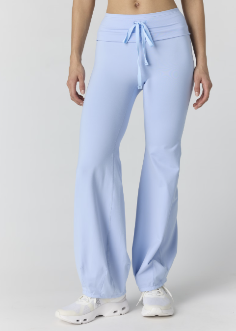 Woman wearing light blue tank and pants on plain background