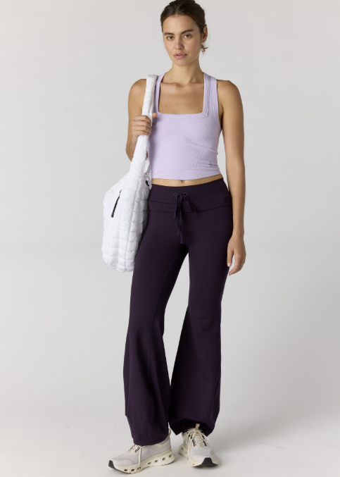 Woman wearing light purple tank and dark purple pants on plain background