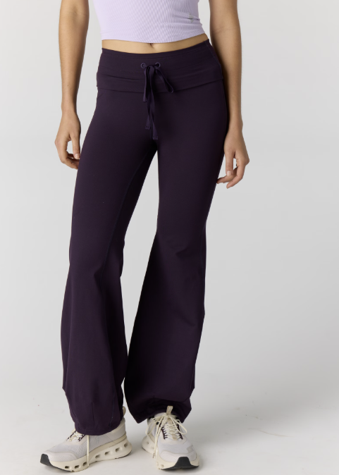 Woman wearing light purple tank and dark purple pants on plain background