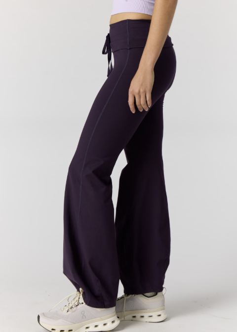 Woman wearing light purple tank and dark purple pants on plain background