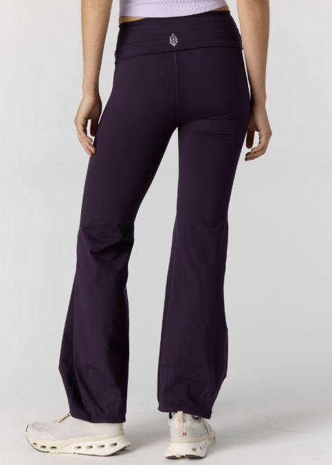 Woman shown from back wearing light purple tank and dark purple pants on plain background