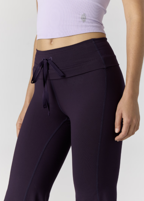 Woman wearing light purple tank and dark purple pants on plain background