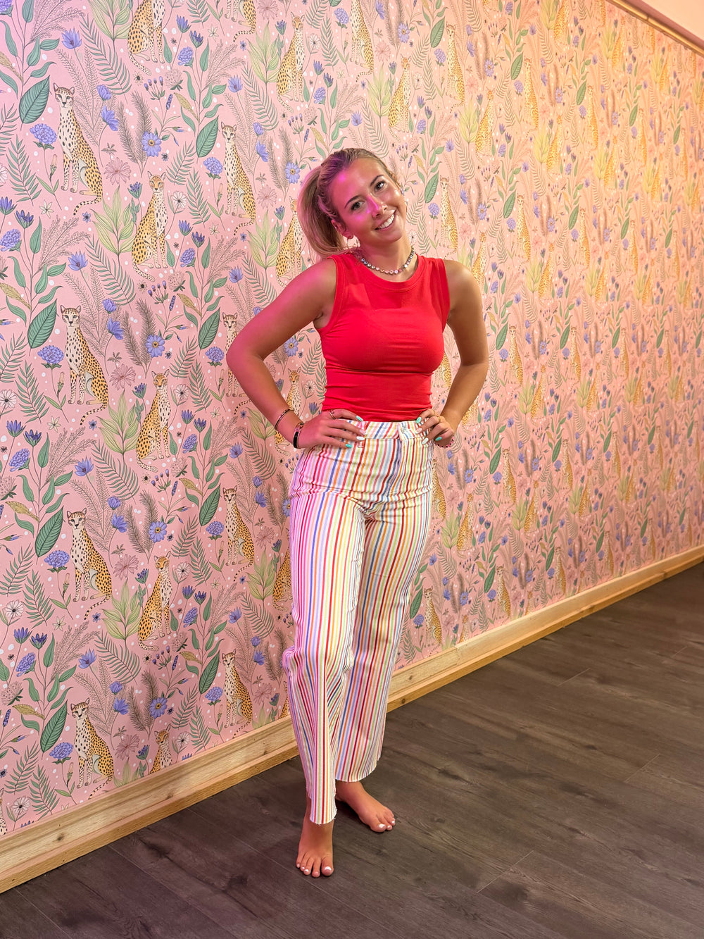 Woman in a red top and colorful pants standing against a patterned wall.