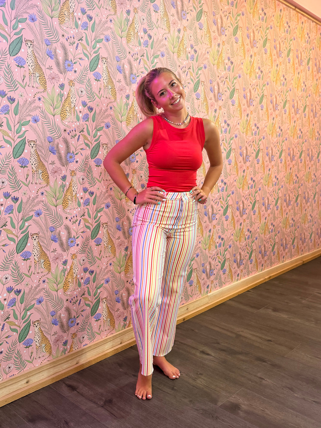 Woman in a red top and colorful pants standing against a patterned wall.