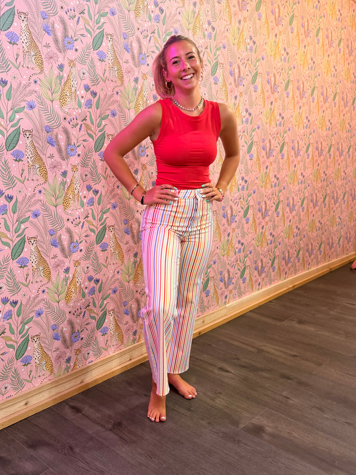 Woman in a red top and striped pants standing against a patterned wall.