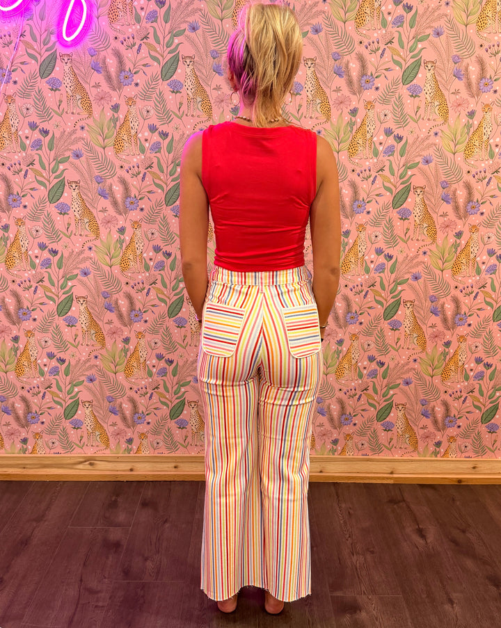 Person wearing a red top and colorful striped pants standing in front of a patterned wall.
