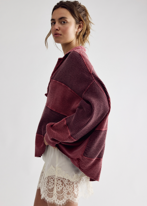 A woman wearing a textured, patchwork-style burgundy corduroy jacket over a white lace-trimmed skirt, photographed against a plain light gray studio background.