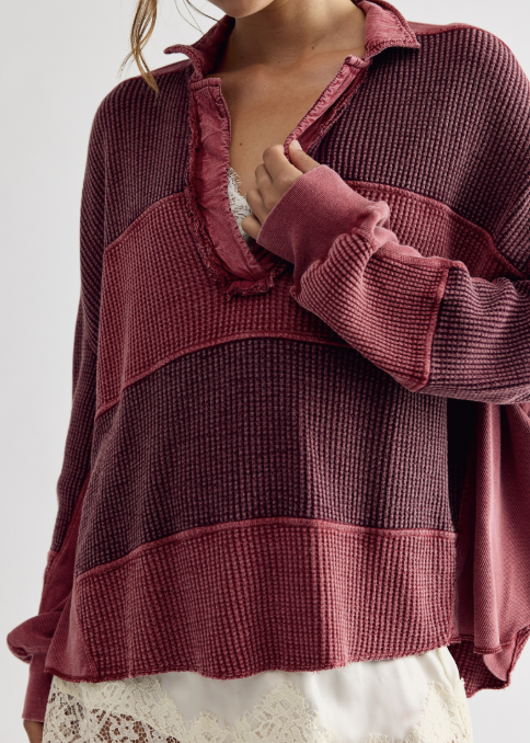 A close-up of a woman wearing a textured waffle-knit long-sleeve top in a dusty rose and dark burgundy color-blocked design, paired with a white lace underlayer.