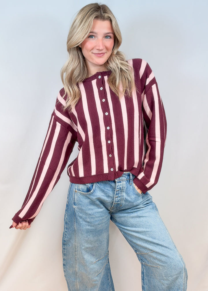 Woman wearing burgundy and pink cardigan with jeans on plain background