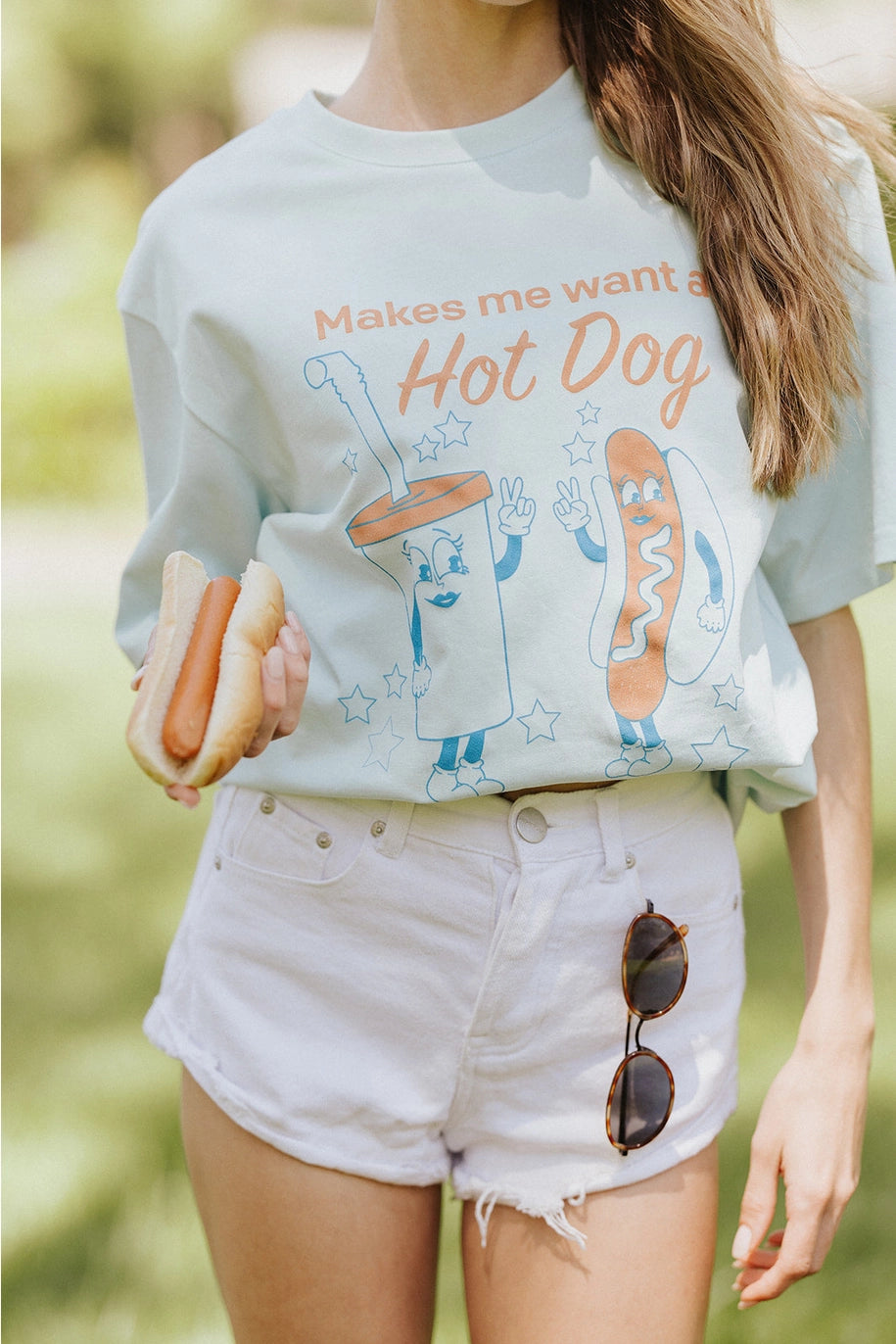 Woman wearing graphic tee with hot dog and drink standing outdoors