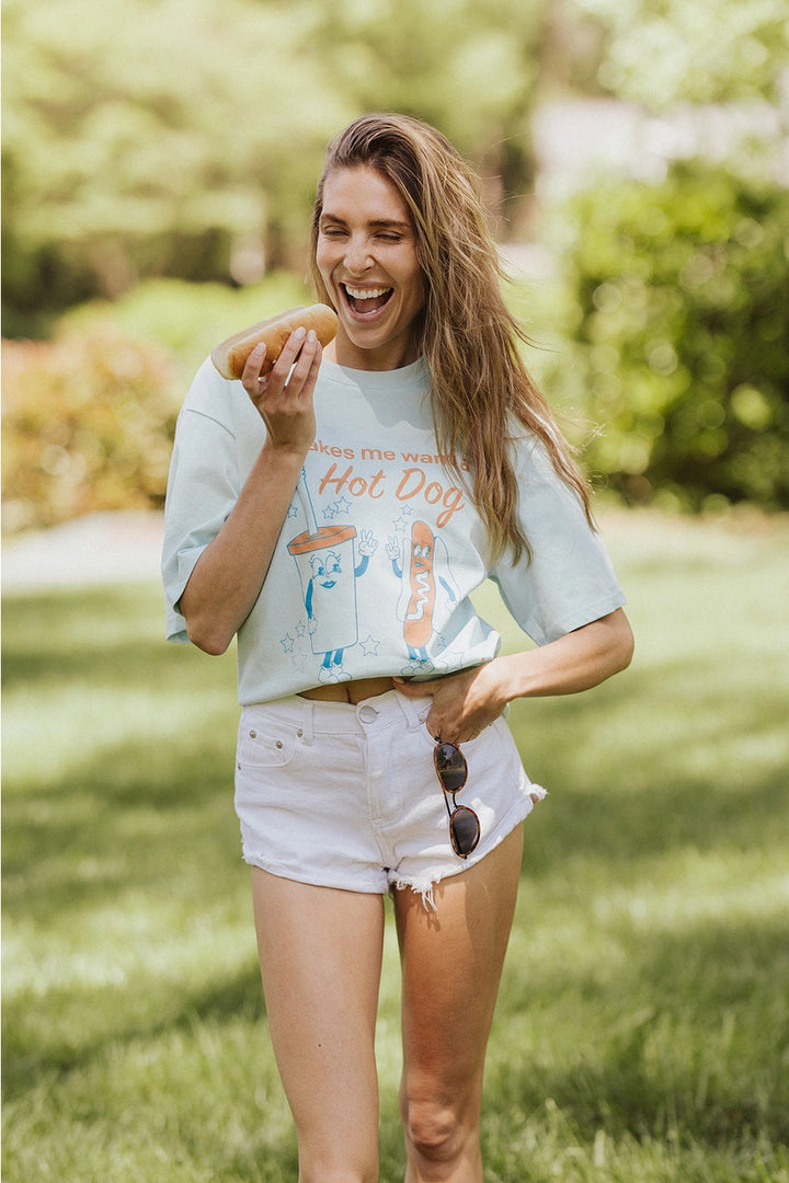 Woman wearing graphic tee with hot dog and drink while eating hot dog