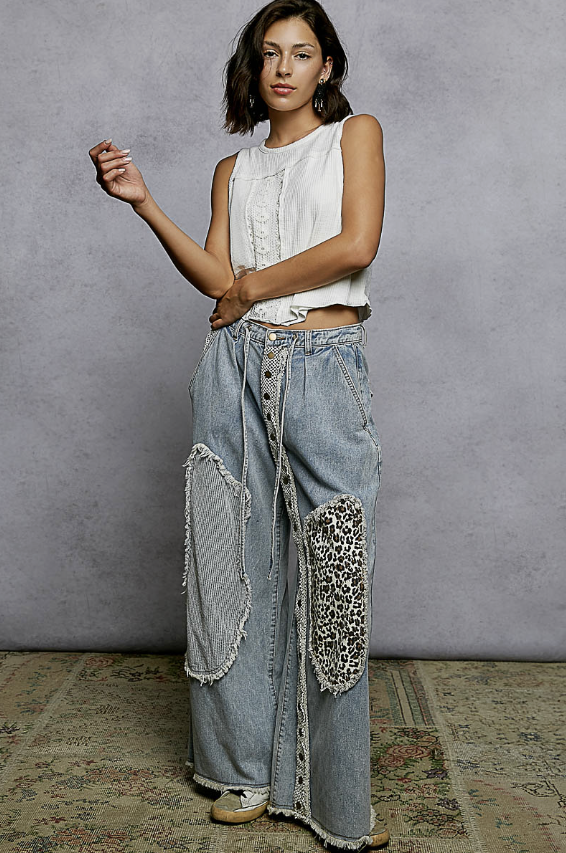 Woman wearing patchwork jeans and white tank on plain background