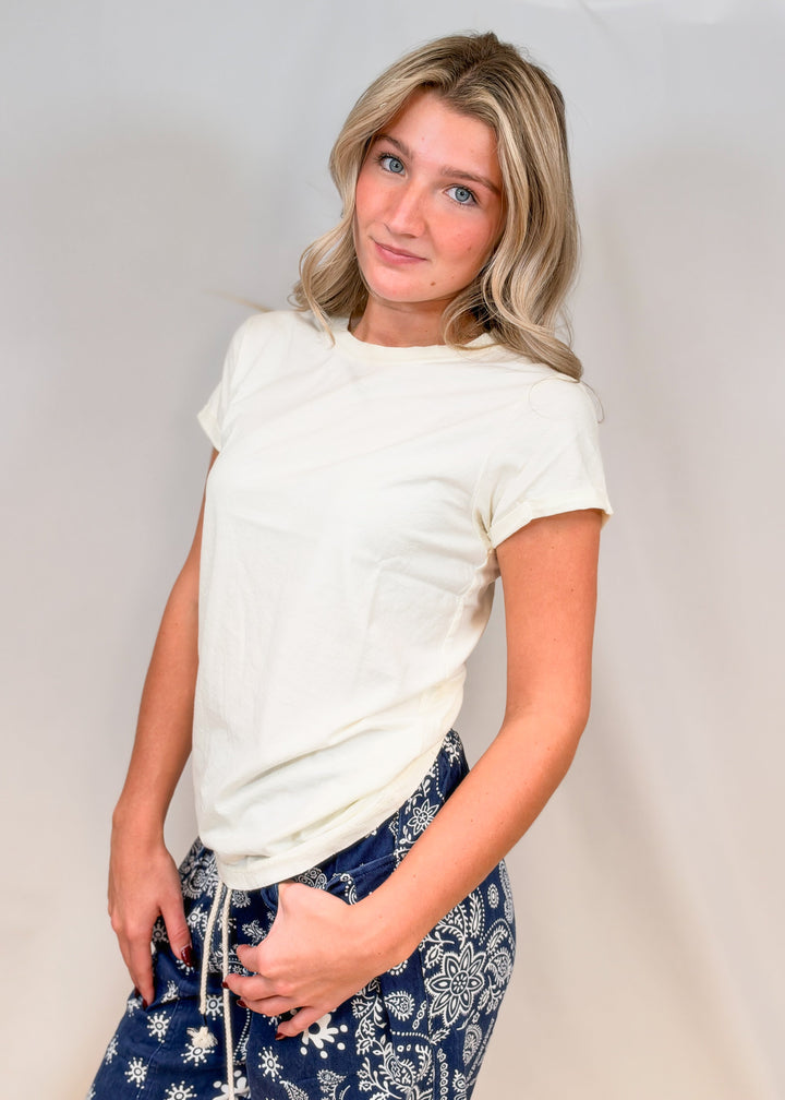 Woman wearing cream fitted tee with blue paisley pants on plain background
