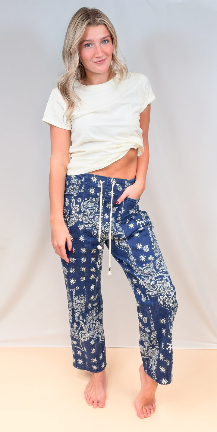 Woman wearing cream fitted tee with blue paisley pants on plain background