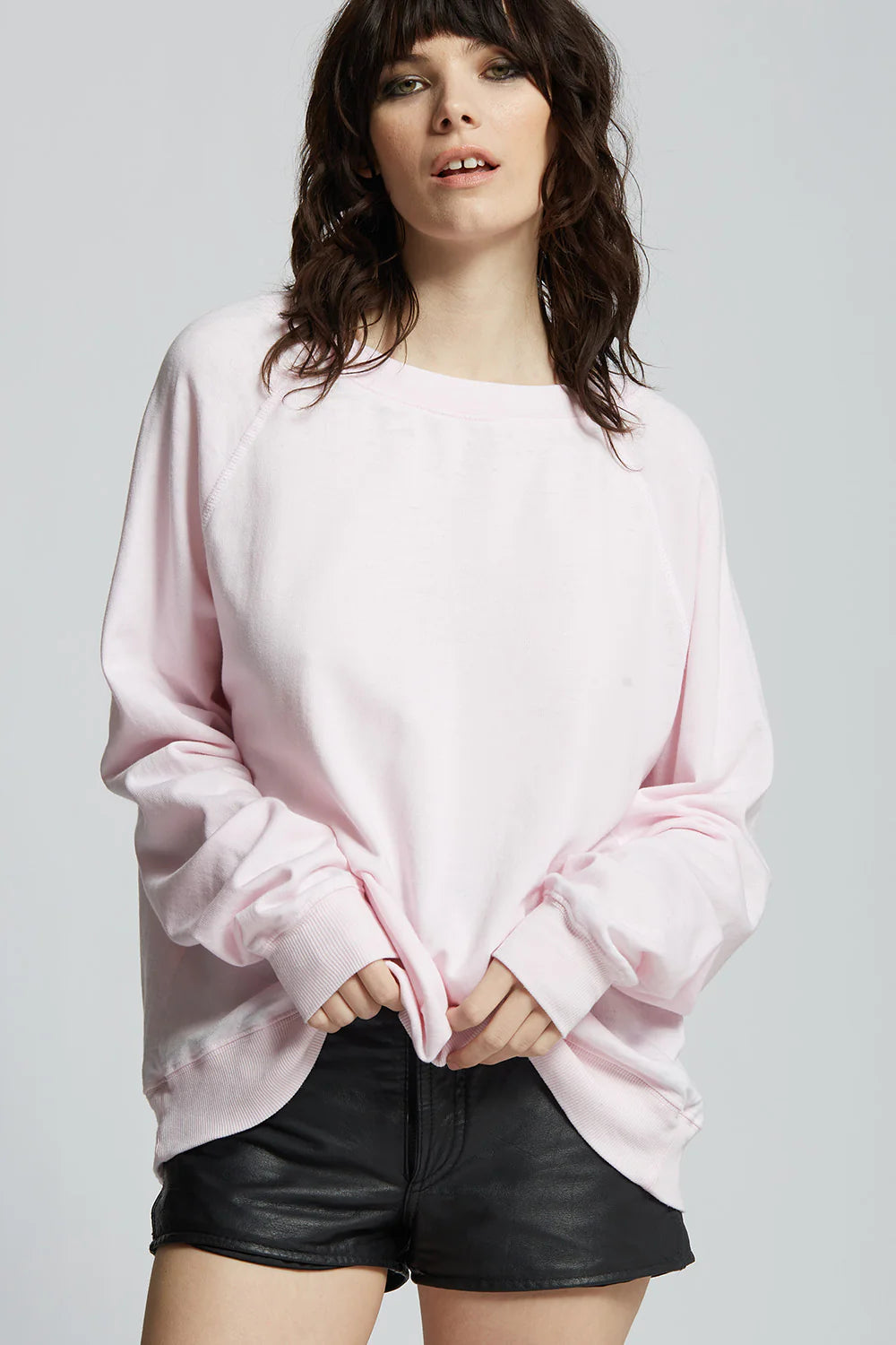 Woman wearing pink sweatshirt and black shorts on plain background