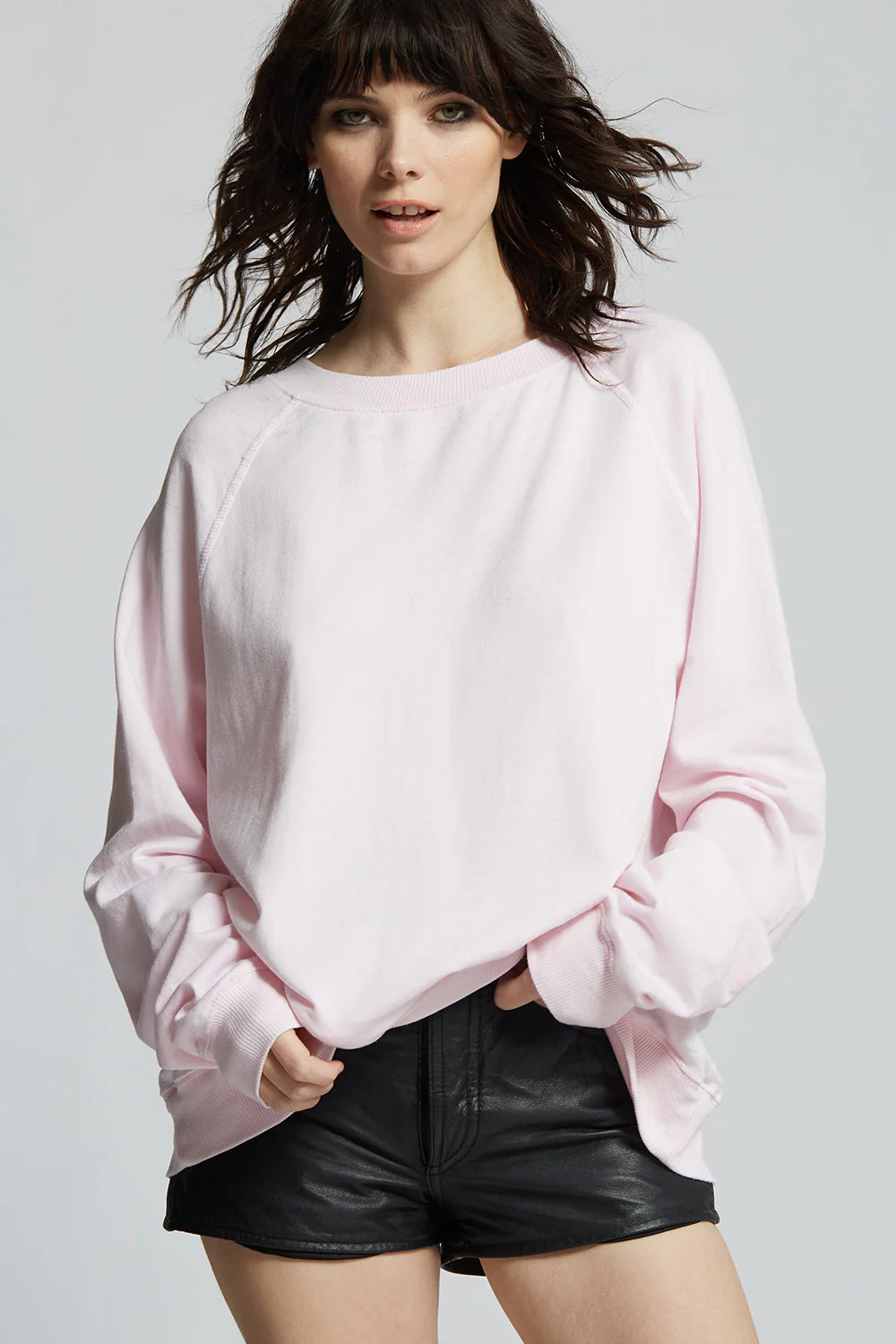 Woman wearing a light pink sweatshirt and black shorts on a plain background