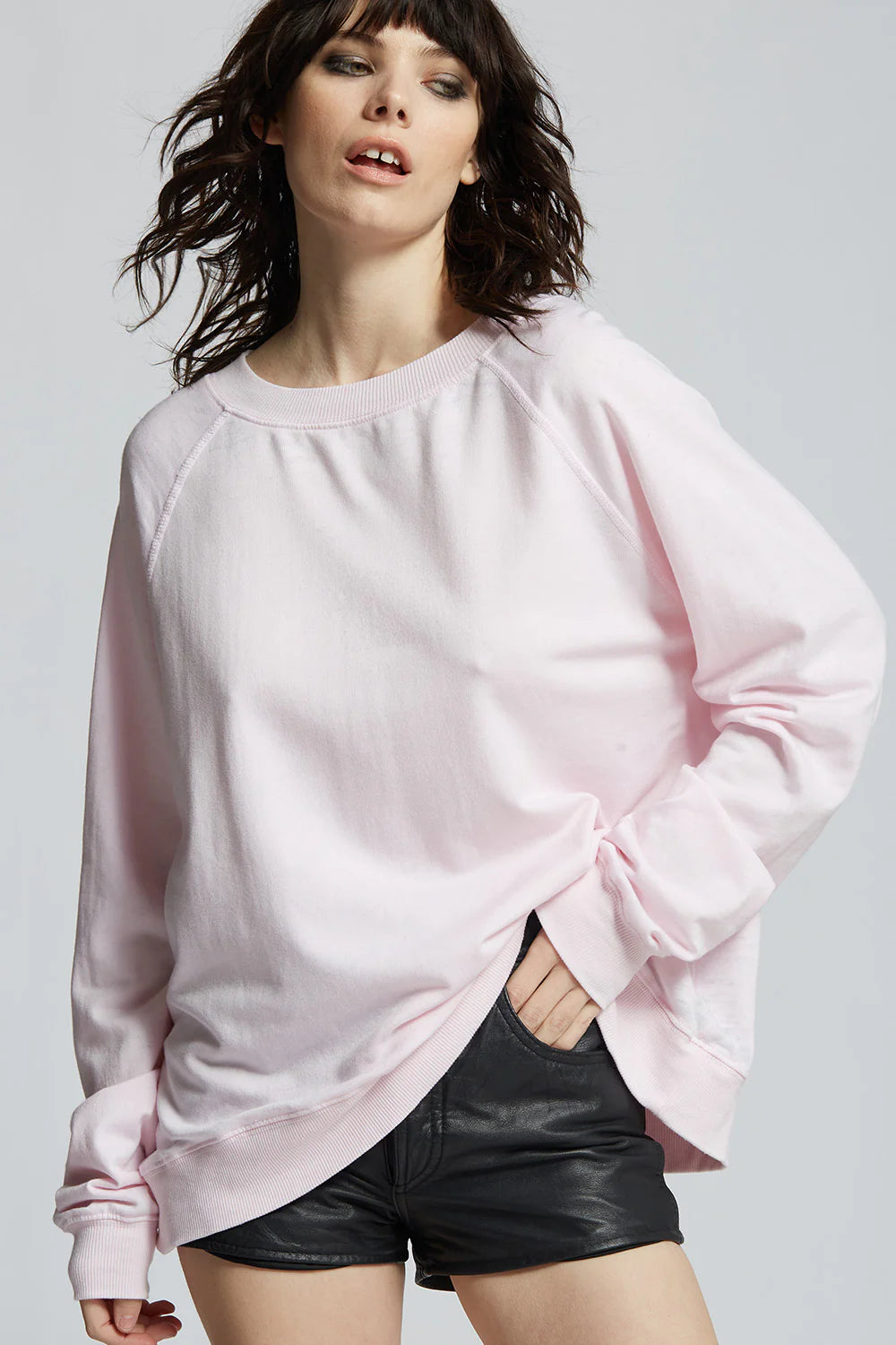 Woman wearing a light pink oversized sweatshirt and black shorts on a plain background
