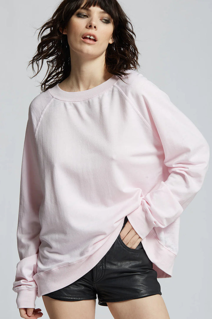 Woman wearing a light pink oversized sweatshirt and black shorts on a plain background