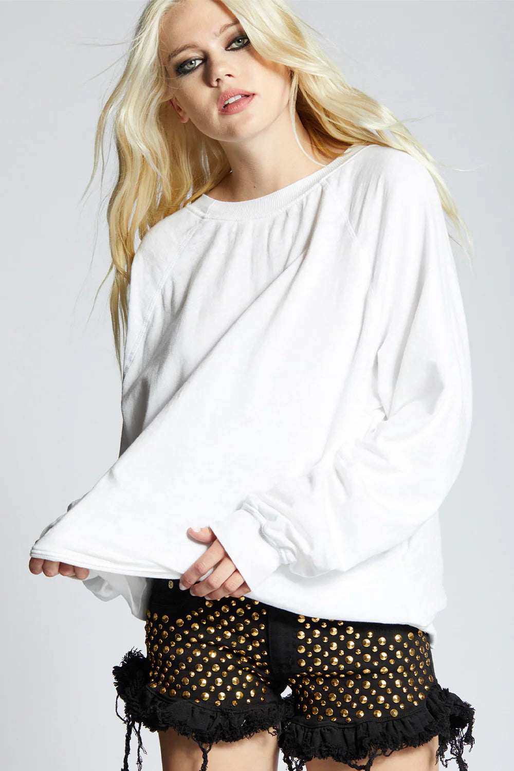 Woman wearing a white top and black shorts with gold accents on a plain background