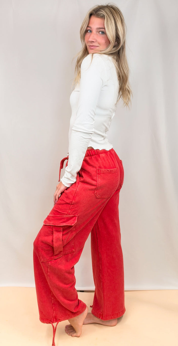Woman shown from side view wearing white top and red pants on plain background