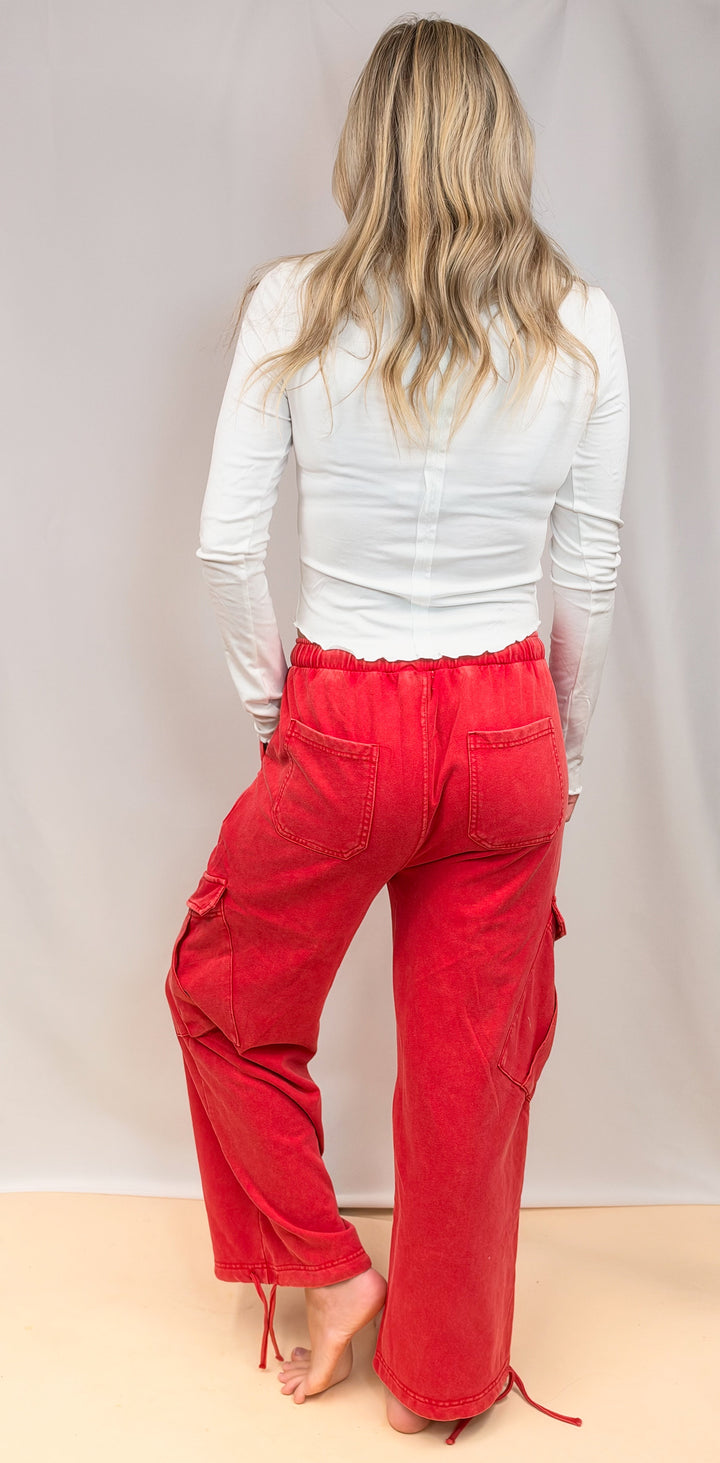 Woman shown from back view wearing white shirt and red pants on plain background